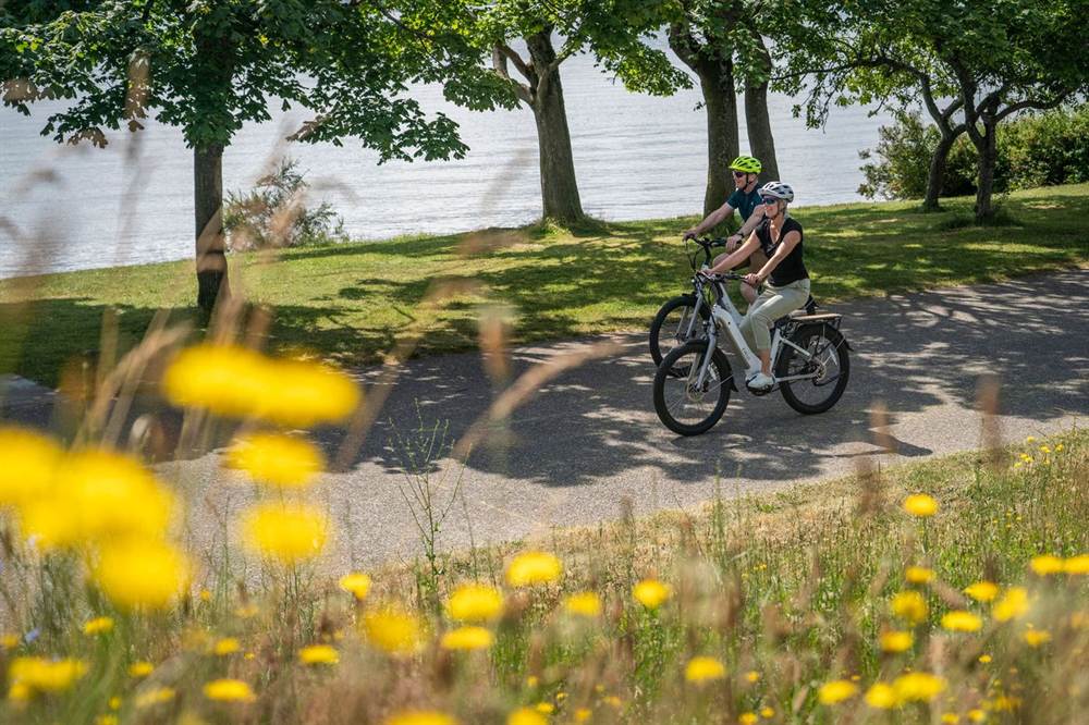 Two riders on e-bikes along a waterside path